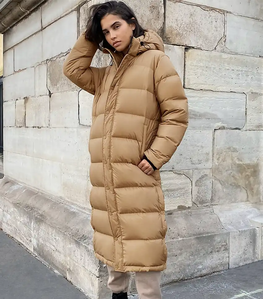 A camel long puffer coat with a hood, worn in a simple street-style look with minimal visible layering.