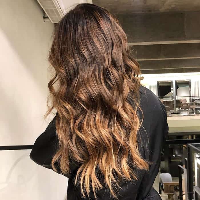 Back view of long wavy hair with dark brown roots melting into caramel-gold ends