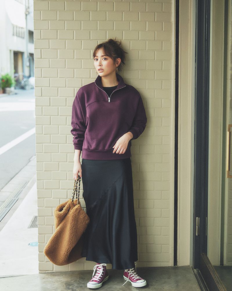 Woman wearing a plum quarter-zip pullover with a black satin maxi skirt, burgundy high-top sneakers and a teddy shoulder bag