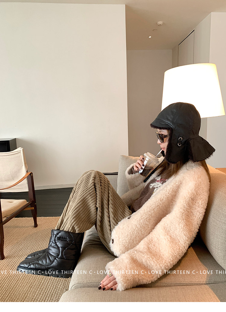 Woman in a cream teddy coat and black leather trapper hat with ribbed wide-leg trousers and snow boots