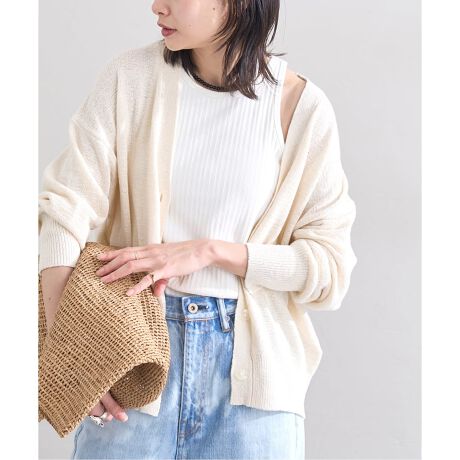 Woman wearing a cream open cardigan over a white ribbed top with light-wash wide-leg jeans, holding a straw clutch