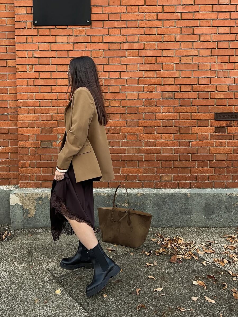 Woman in a camel blazer over a dark slip dress with black chunky Chelsea boots