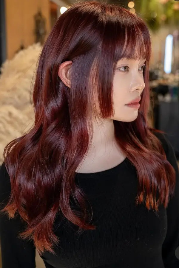 Three-quarter view of long cherry cola hair with wispy curtain bangs and copper-red ends
