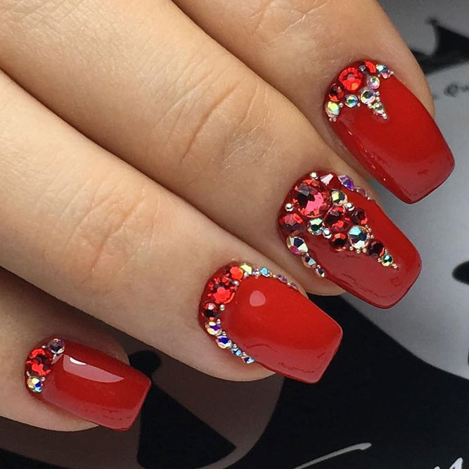 Glossy red nails with rhinestone and crystal accents along the cuticle line