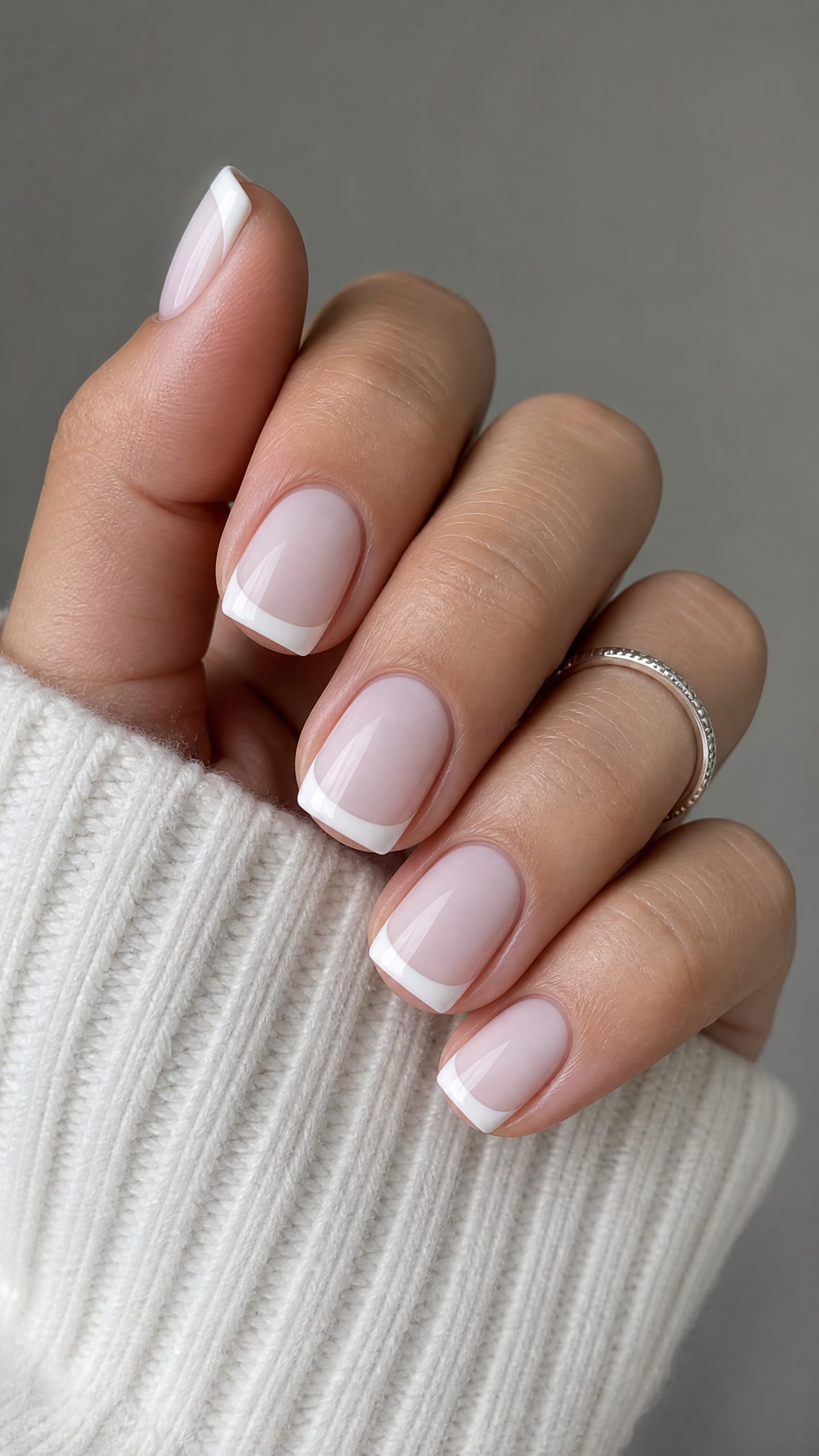 Short rounded nails with classic white French tips on a sheer pink base