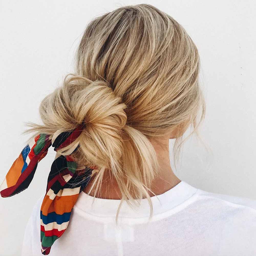Messy blonde low bun with a colorful striped silk scarf tied at its base