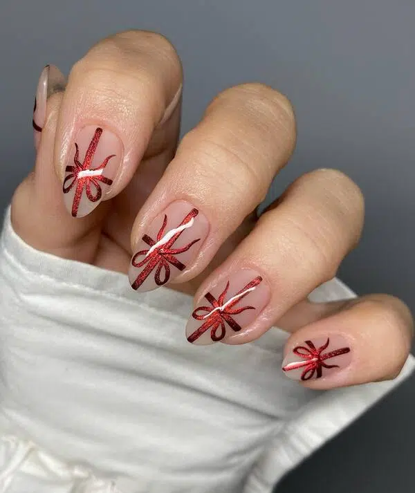 Red glitter bow nail art painted on nude almond nails