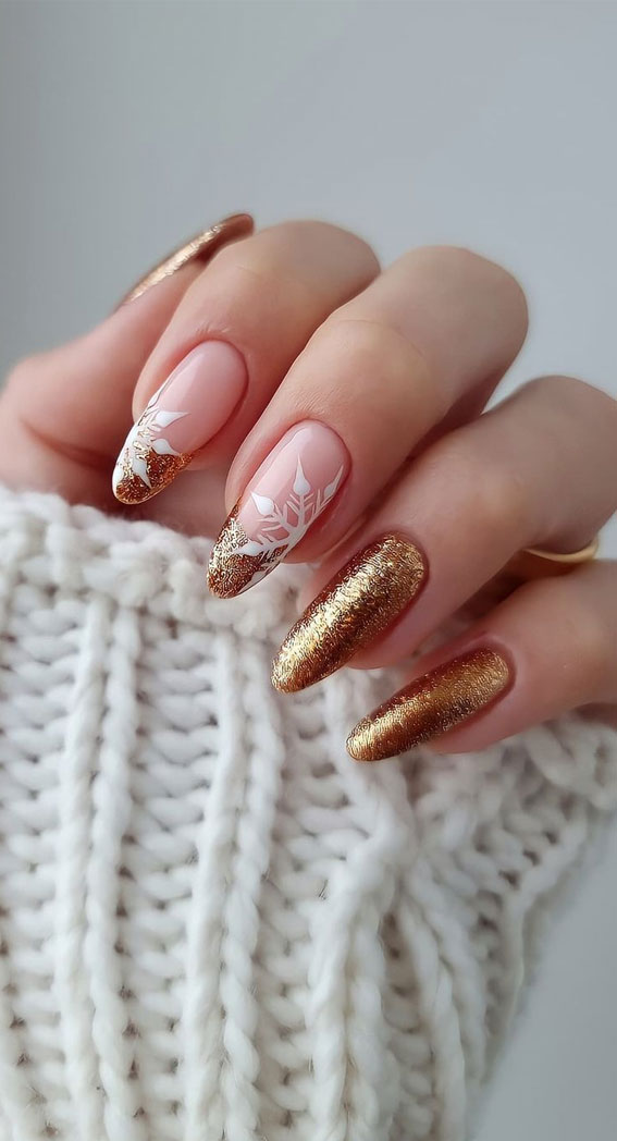 Oval nude nails with champagne-gold glitter accents and white snowflake nail art on the feature nails