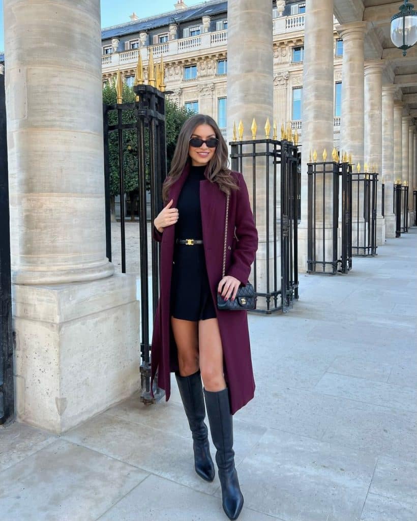 Woman in a burgundy wool coat with a black mini dress, knee-high boots, and a black quilted bag in Paris