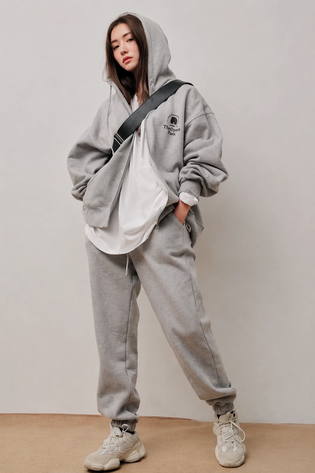 Woman wearing a grey zip-up hoodie over a white tee with matching grey sweatpants and chunky sneakers
