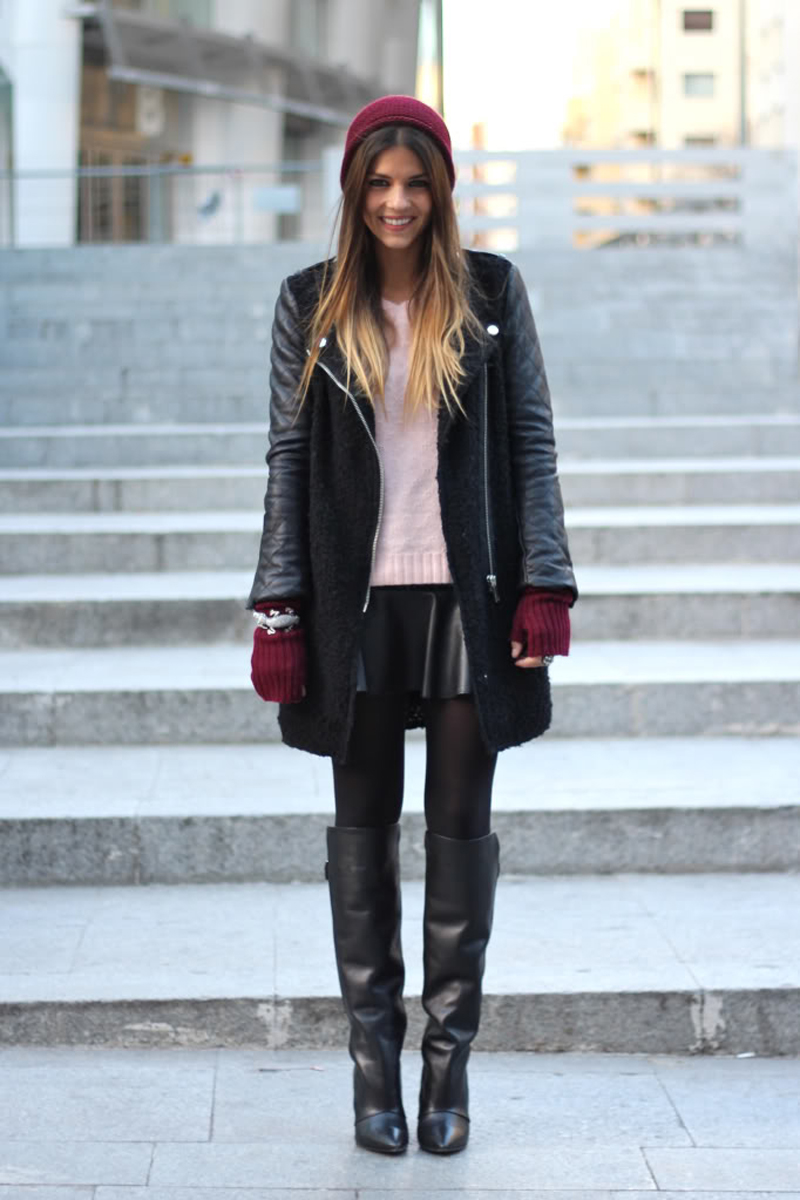 Woman in a burgundy beanie, black coat, blush sweater, black skirt and over-knee boots