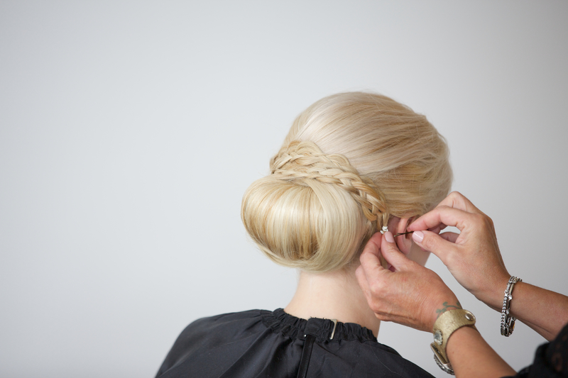 Stylist wrapping a braid around a low bun on blonde hair