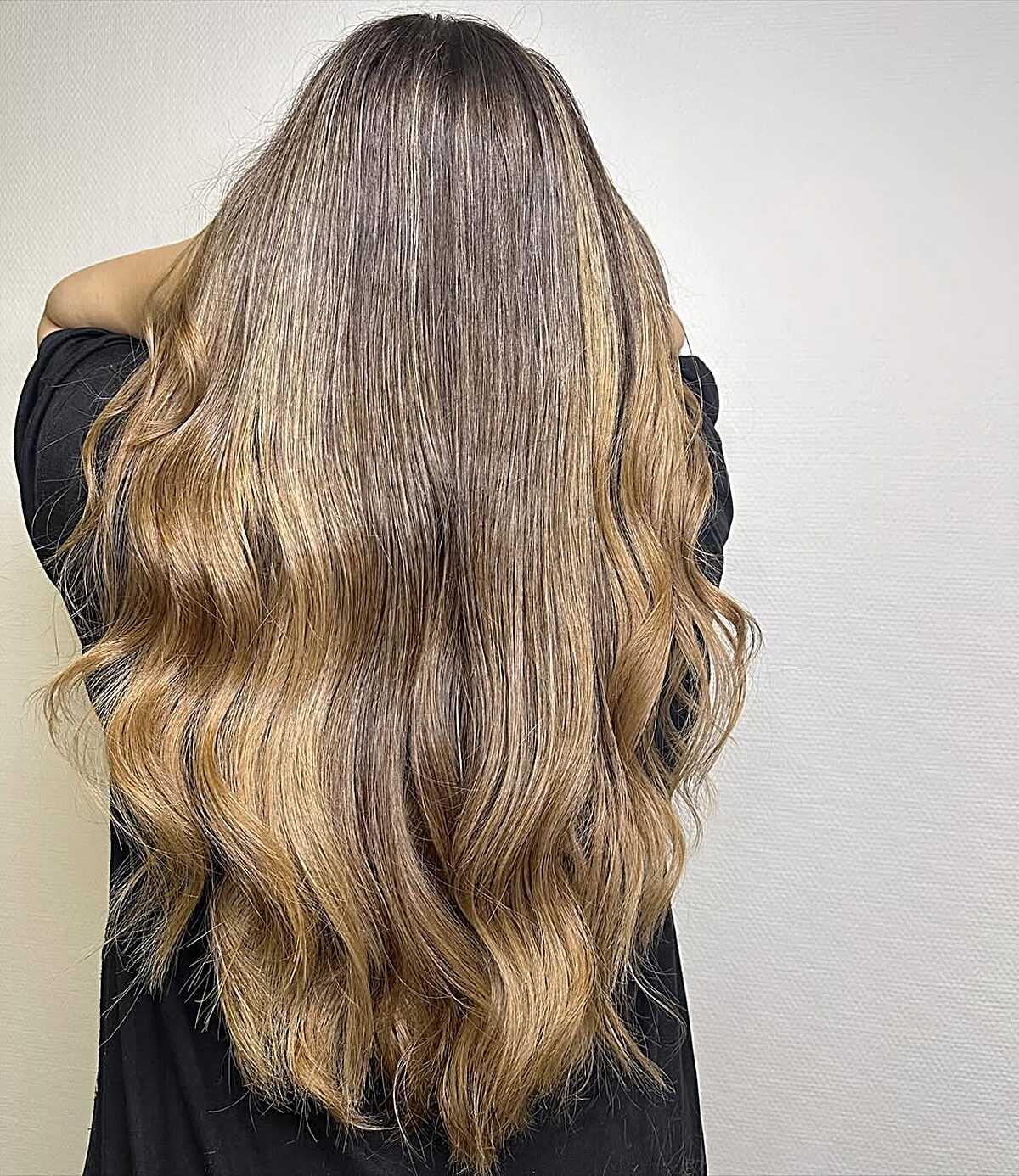 Long loose waves blending cool brown roots into warm honey blonde