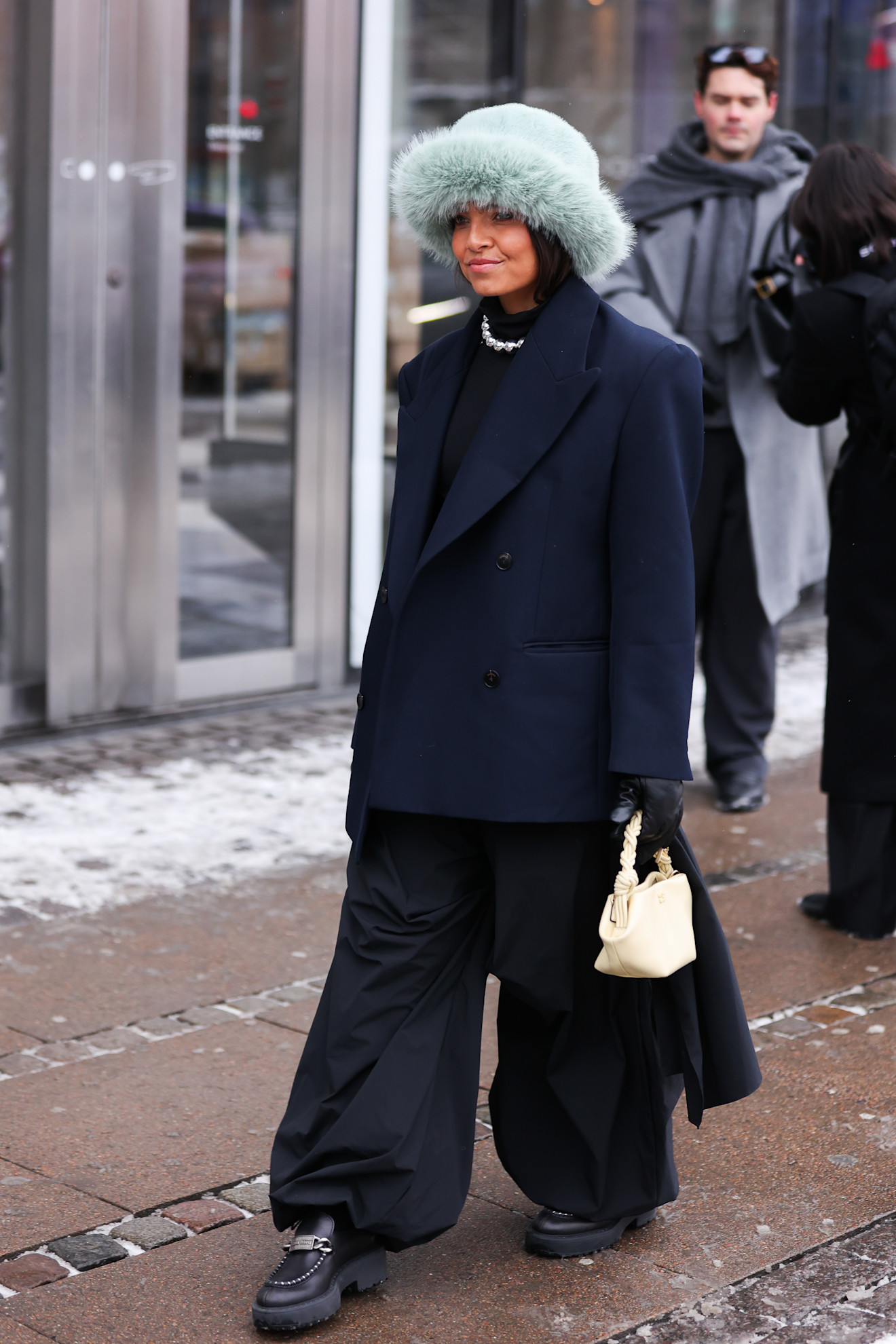 Woman in a mint green faux fur hat, navy blazer and wide-leg black trousers at Copenhagen Fashion Week