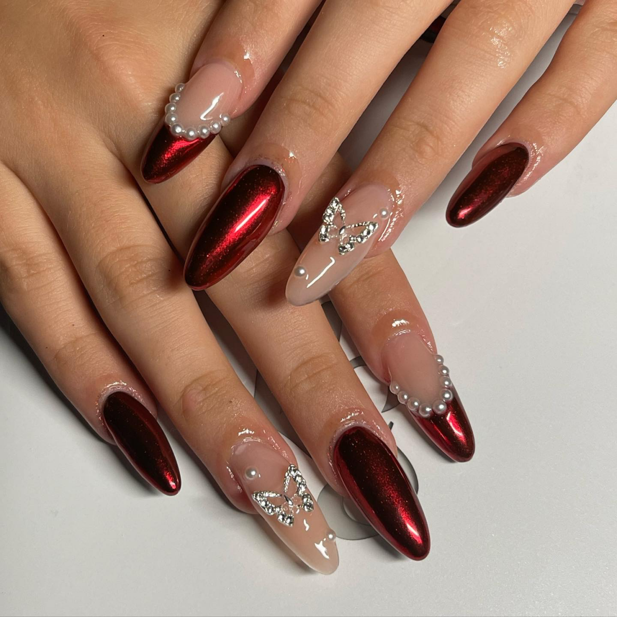 Metallic red chrome nails with pearl French tips and crystal bows