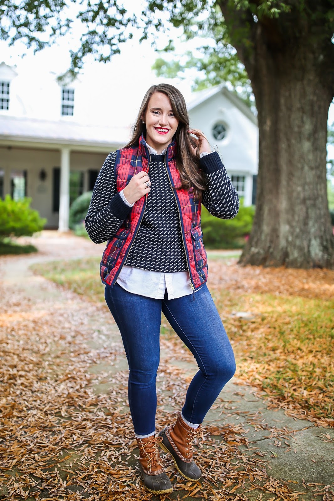 Woman wearing a red plaid quilted vest with a navy sweater, jeans and duck boots