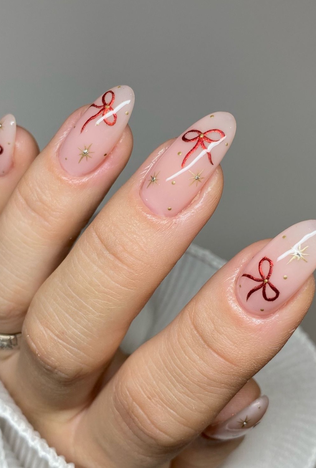 Long almond nude nails with red hand-painted bows and gold starburst accents