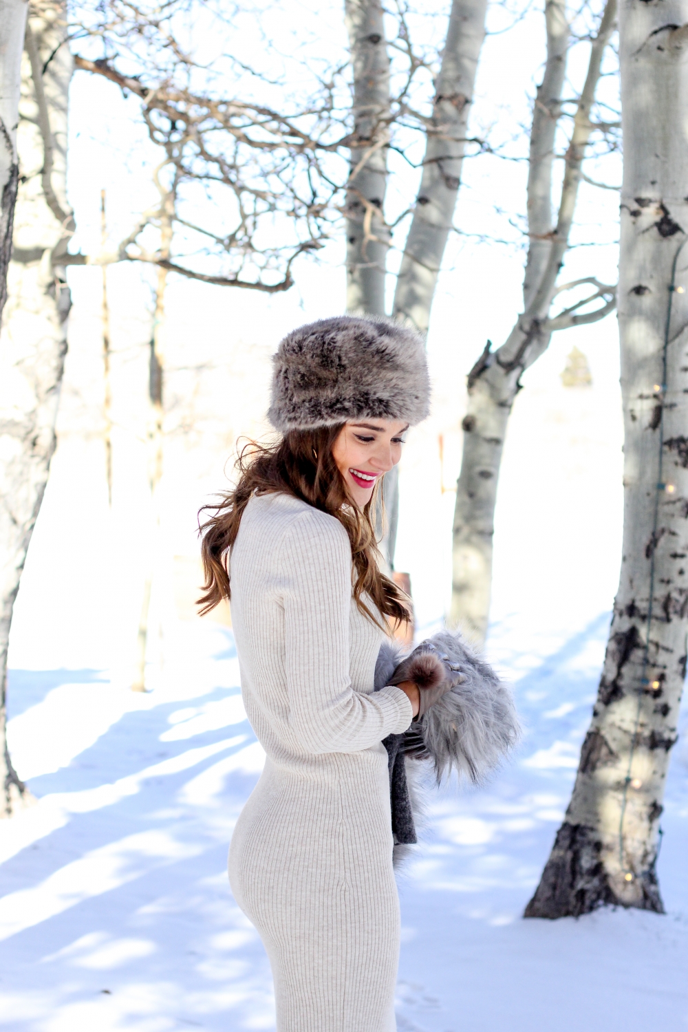 Woman in a grey fur pillbox hat and cream ribbed sweater dress in the snow