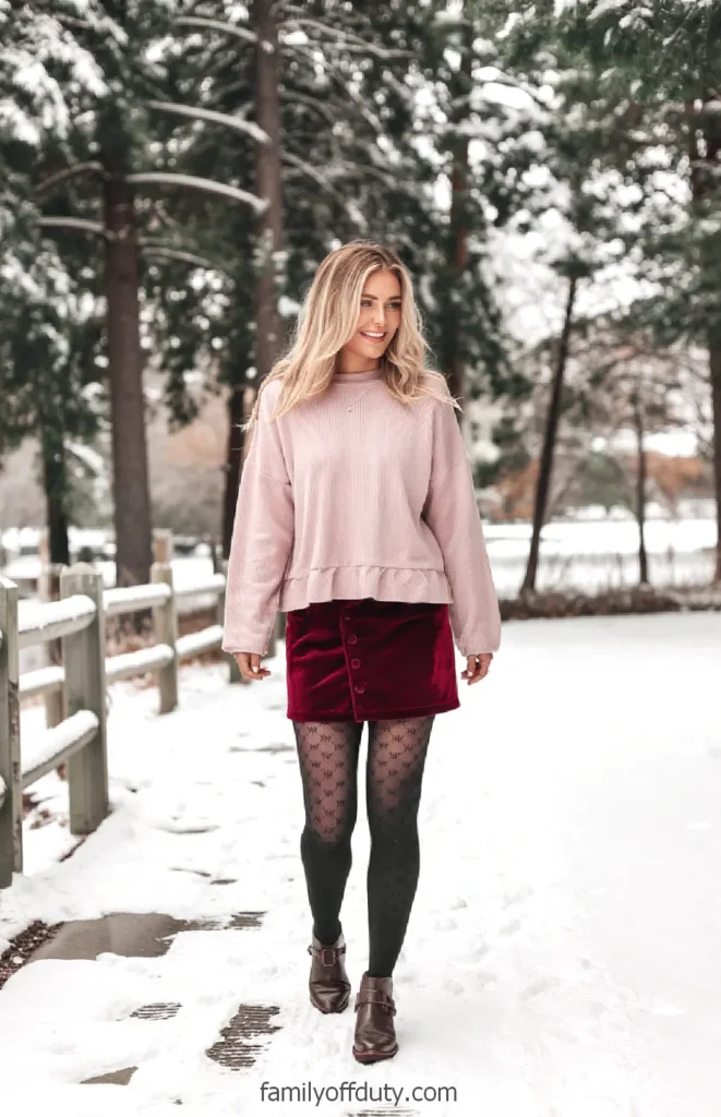Woman in ruffle-hem sweater and velvet skirt with patterned tights on a snowy path