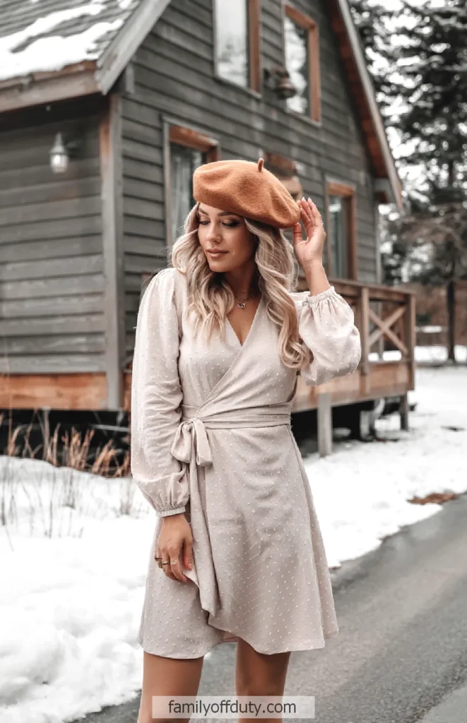 Woman in long-sleeve wrap dress, tights and wool beret by a snowy cabin
