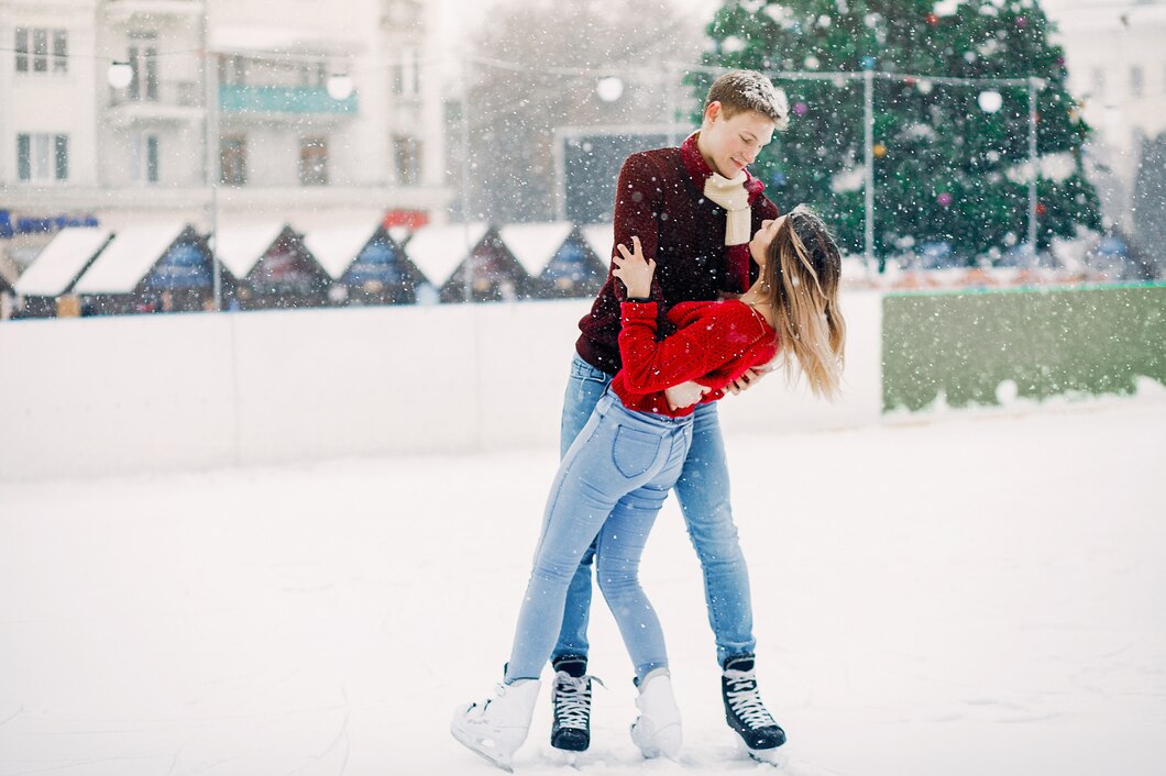 Couple ice skating in the snow, the woman in a red sweater and light jeans and the man in a burgundy knit and jeans