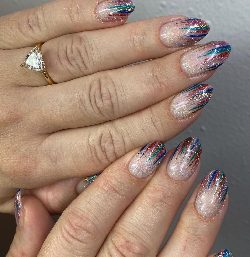 Almond nails in sheer nude with multicolor metallic tinsel streaks in red, blue, gold and green glitter