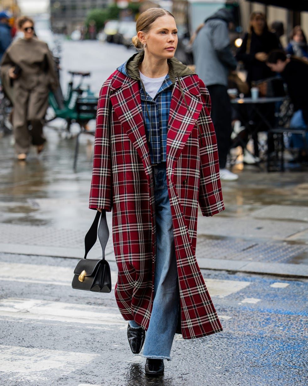 Woman in a red plaid long coat layered over a blue plaid shirt with jeans, black boots and a black handbag