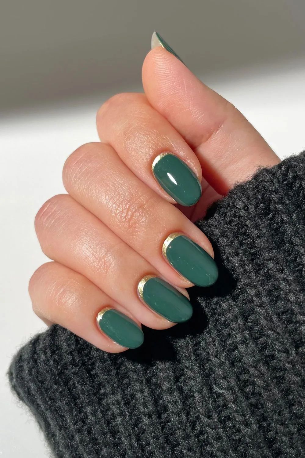 Short almond deep pine green nails with thin gold half-moon accents at the cuticles
