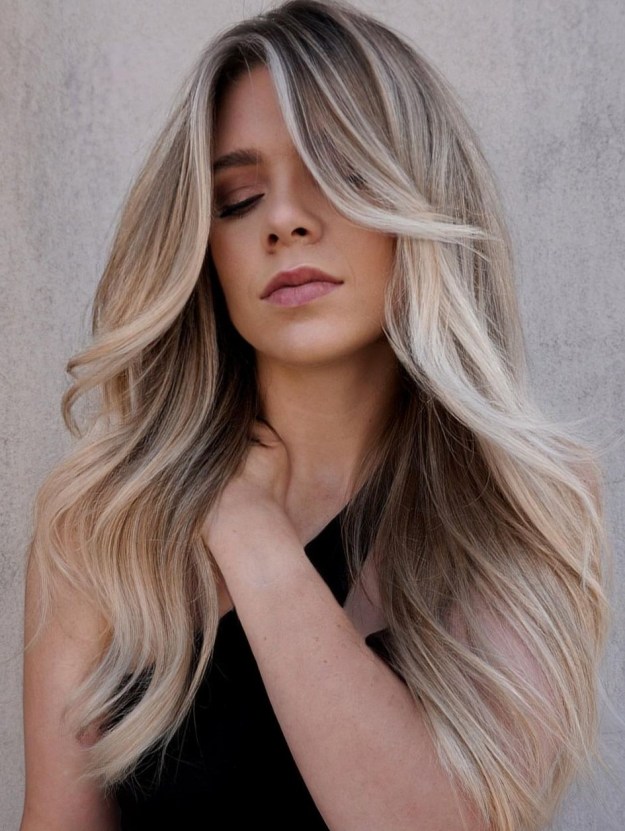 Dark blonde hair with a smudged root and long layered waves