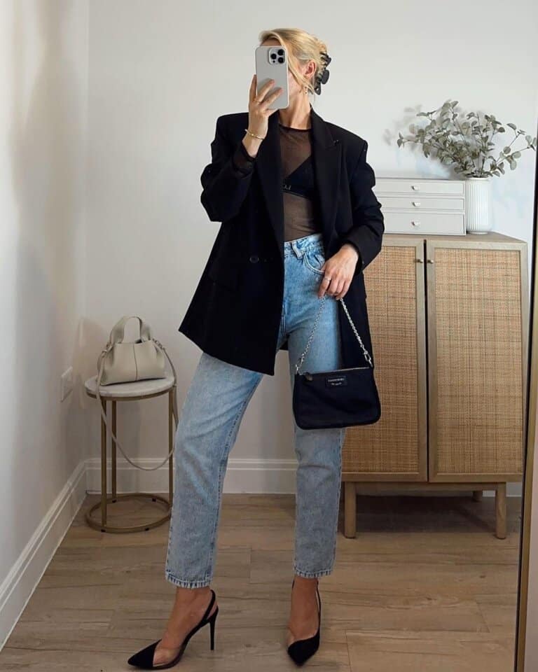 Woman in a black oversized blazer with a sheer black top, light-wash jeans and black pointed heels