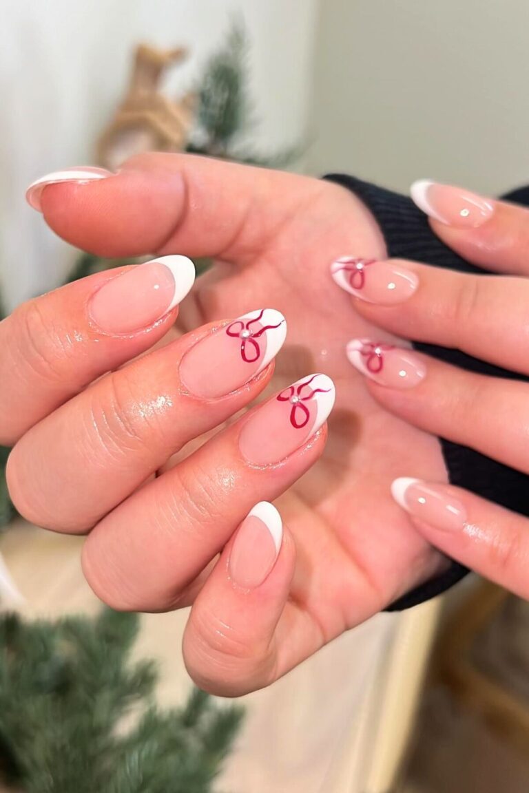 Almond nails with classic white French tips and small red bows painted near the cuticles