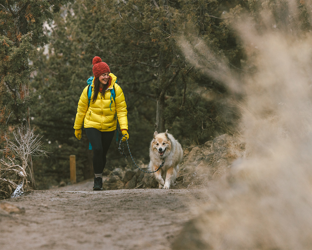 Woman hiking a snowy trail with her dog near a volcanic butte