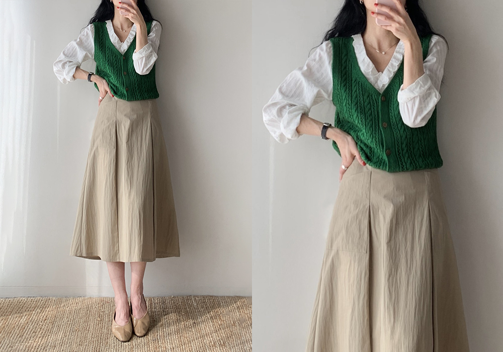 Woman in a green cable-knit vest over a white blouse with a beige midi skirt and beige flats, shown in a mirror selfie