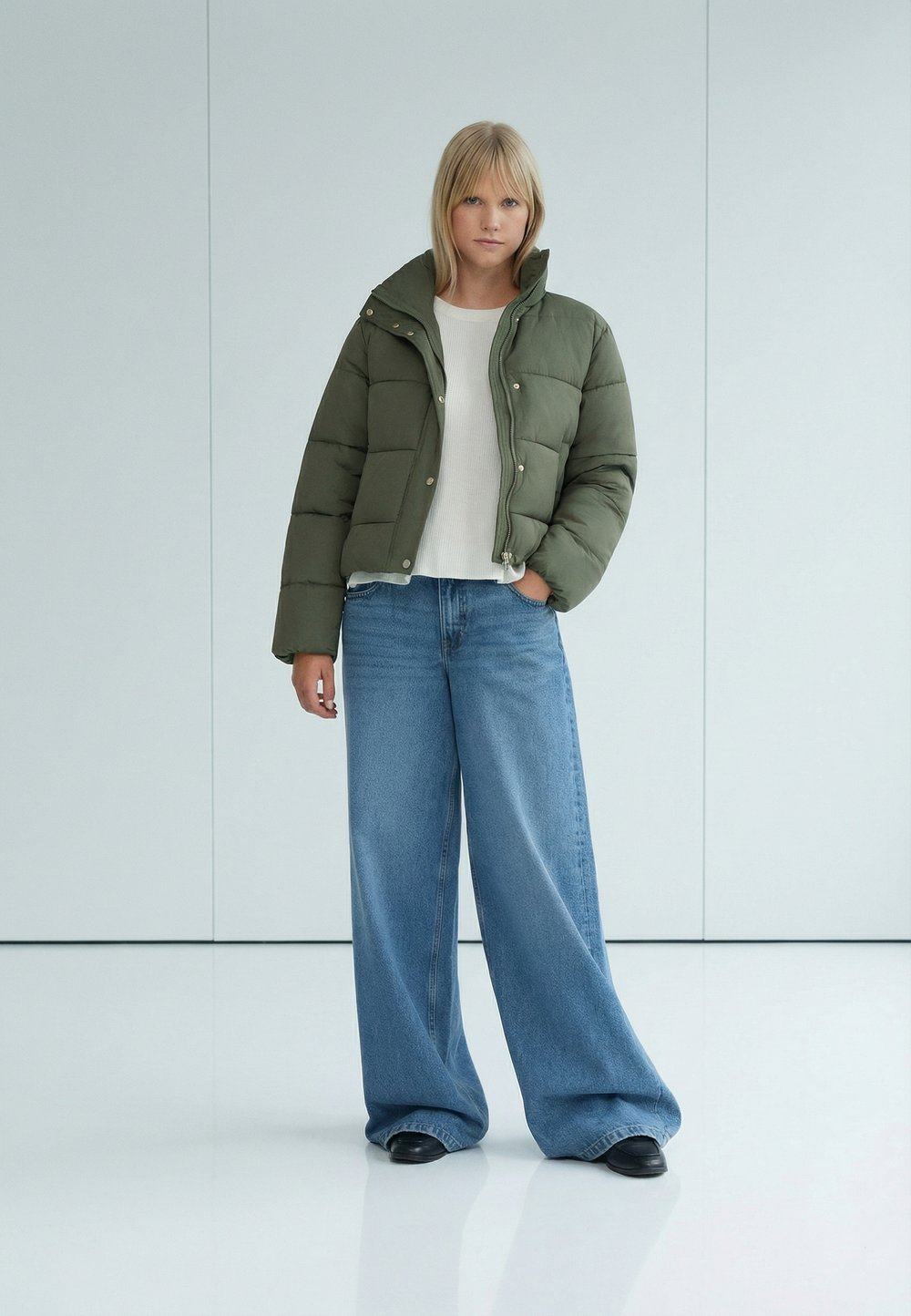 Woman in an olive cropped puffer jacket with a white ribbed top and wide-leg jeans