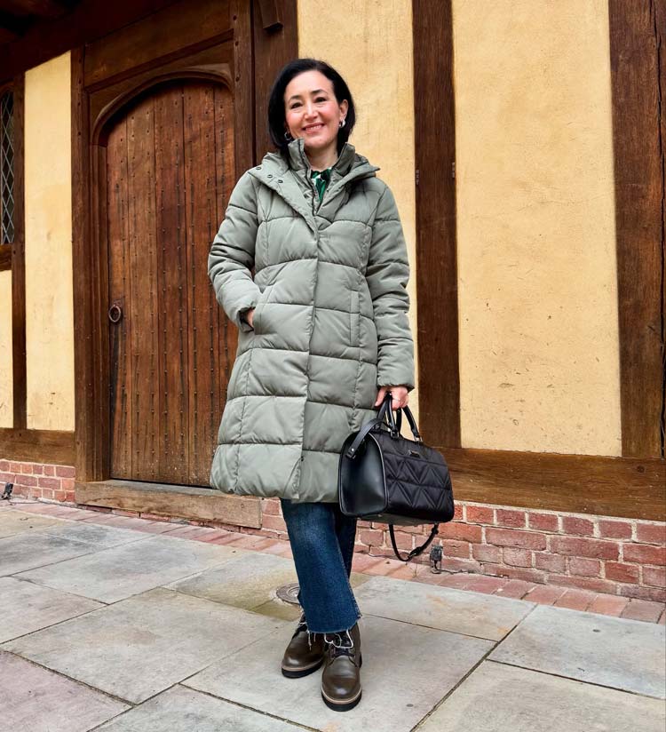 Woman in a sage green mid-length puffer with dark jeans and brown lace-up boots