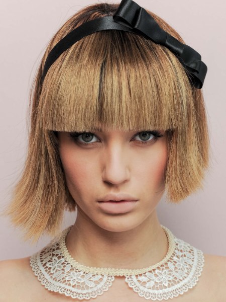 Woman with a short blonde bob and blunt bangs wearing a black bow headband