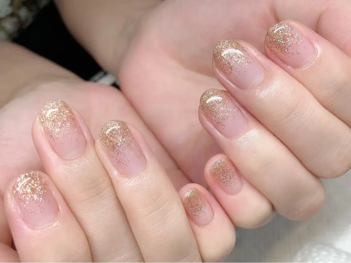 Short oval nails with champagne gold glitter fading from the tips over a sheer nude base