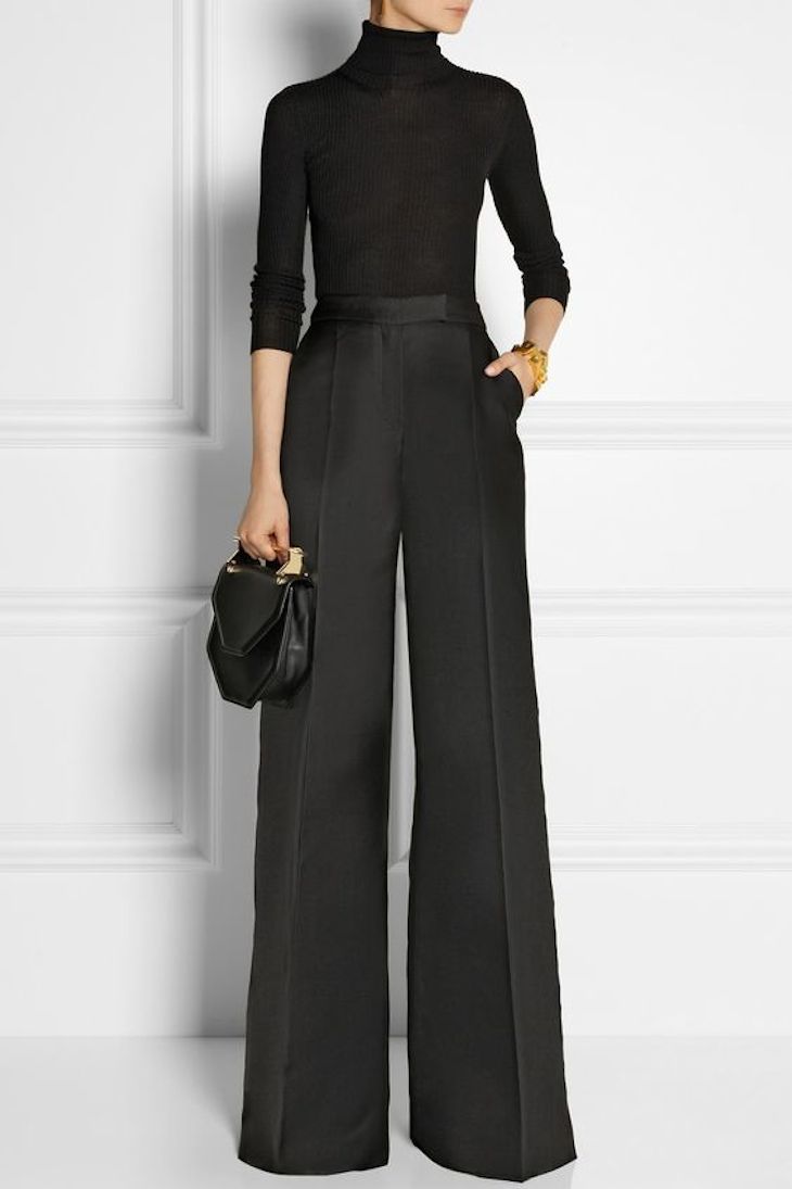 Woman in a fitted black turtleneck bodysuit tucked into high-waist black wide-leg trousers with a small bag and gold cuff