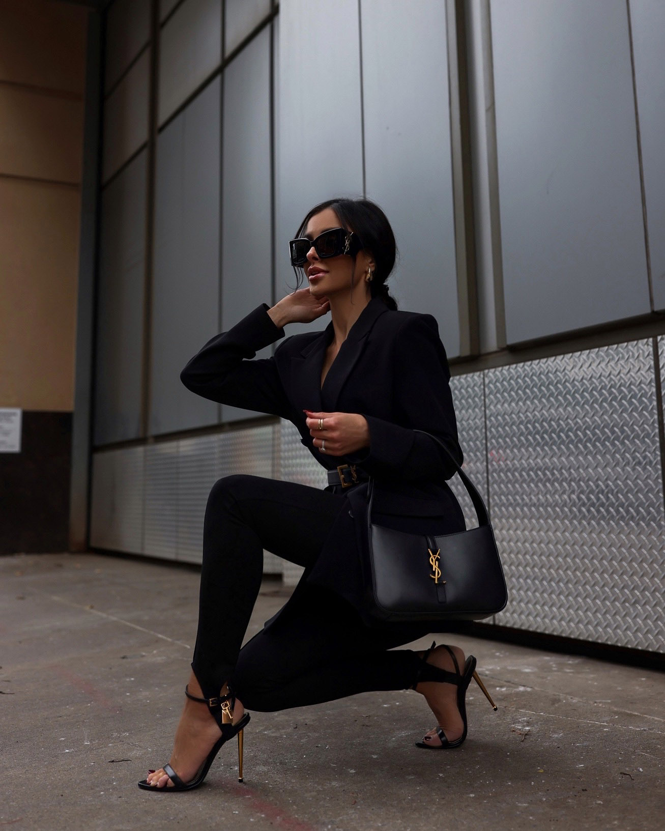 Woman in a black blazer and black leggings with strappy heeled sandals, a black handbag and sunglasses