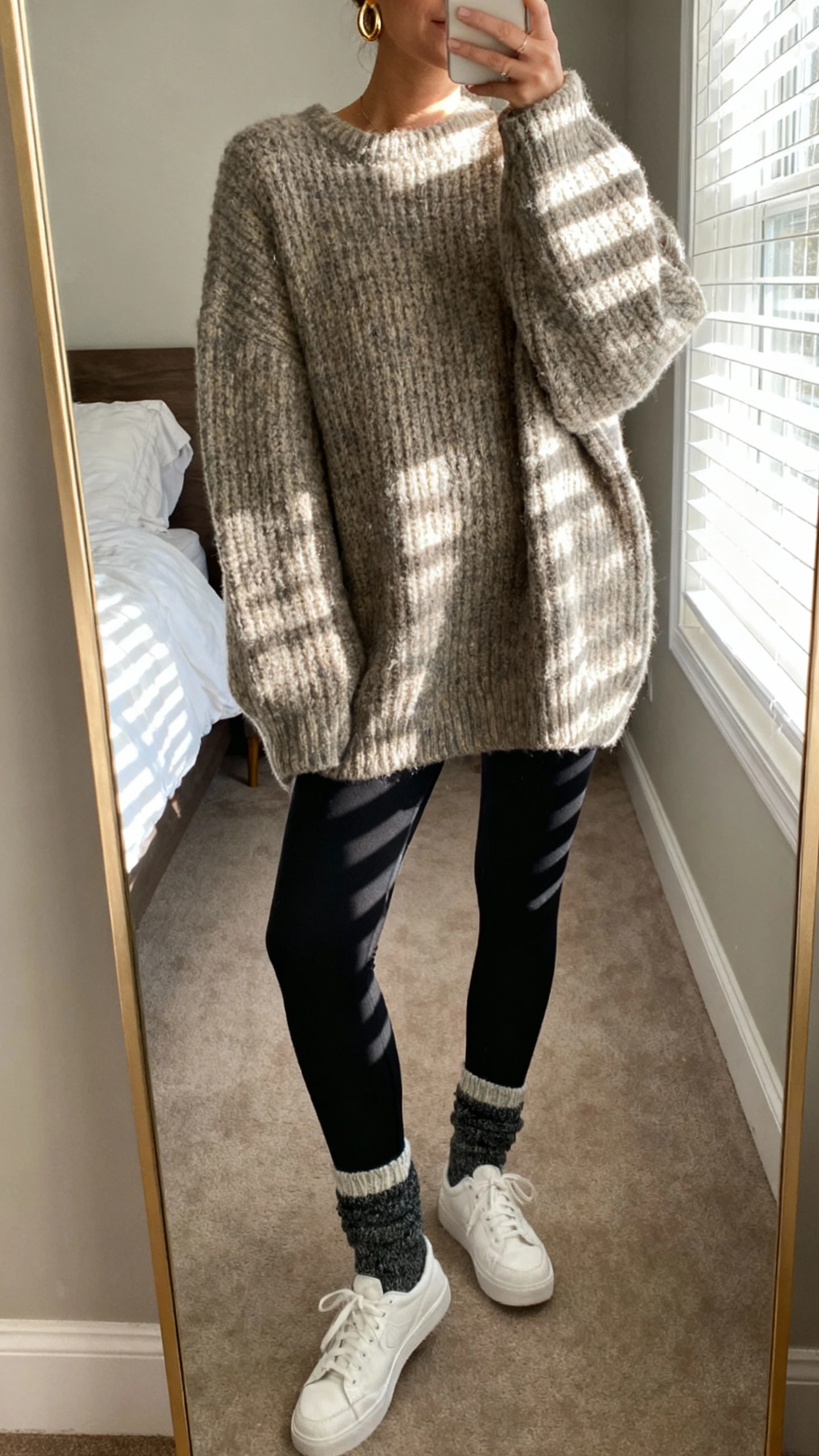 Woman wearing an oversized oatmeal chunky knit sweater with black leggings, knit socks and white sneakers