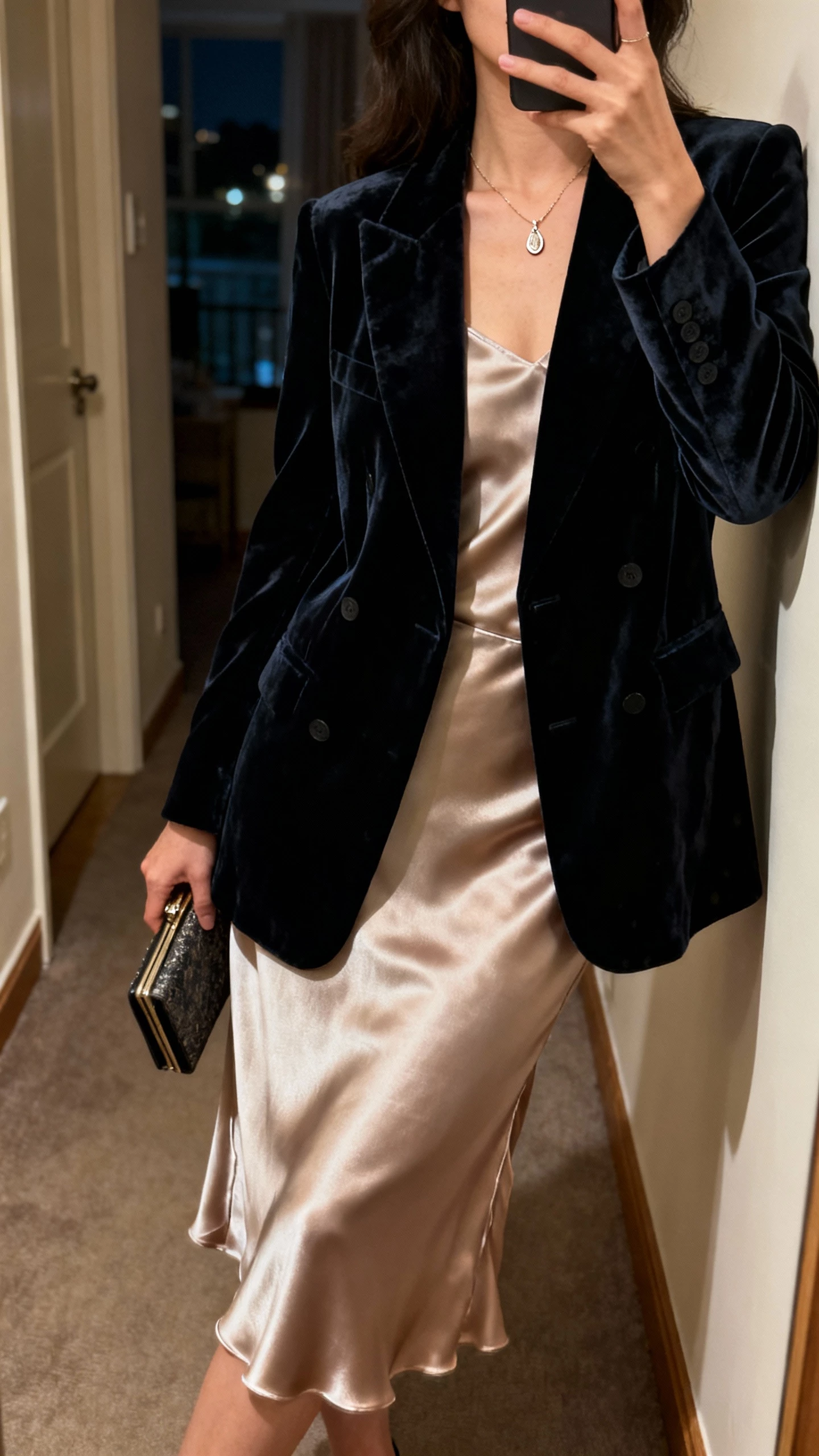 Woman in a navy velvet double-breasted blazer over a champagne satin slip dress holding a sparkly clutch