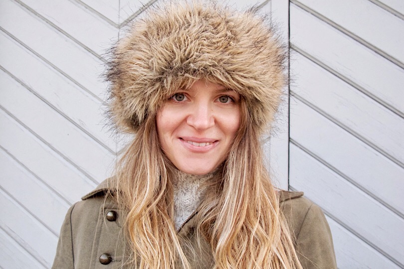Close-up of a woman wearing a tan faux fur hat with an olive coat