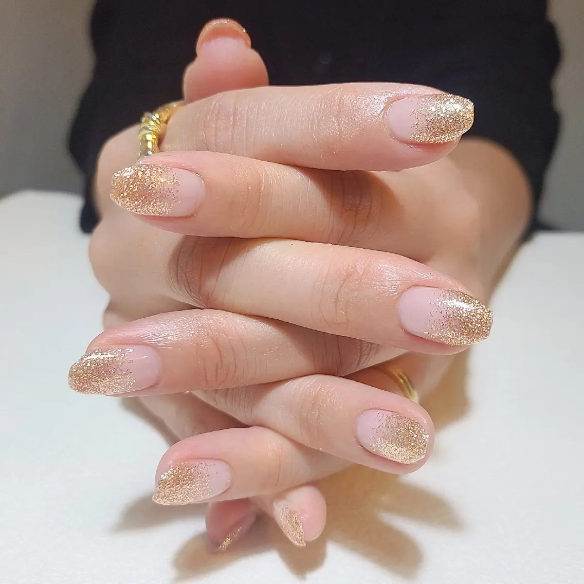 Short oval nude nails with fine gold glitter fading from the tips