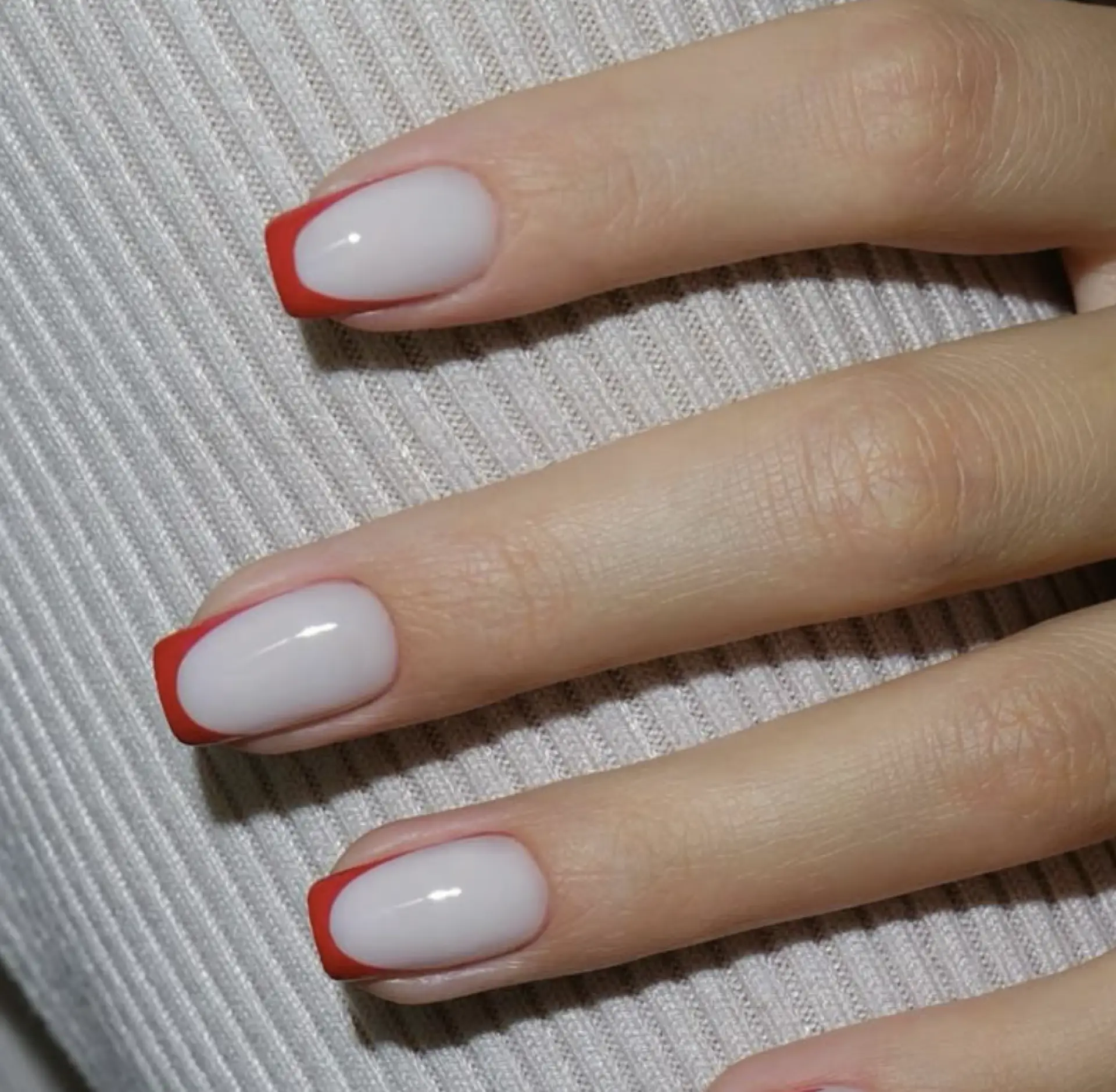 Short square nails with a milky white base and thin red French tips.