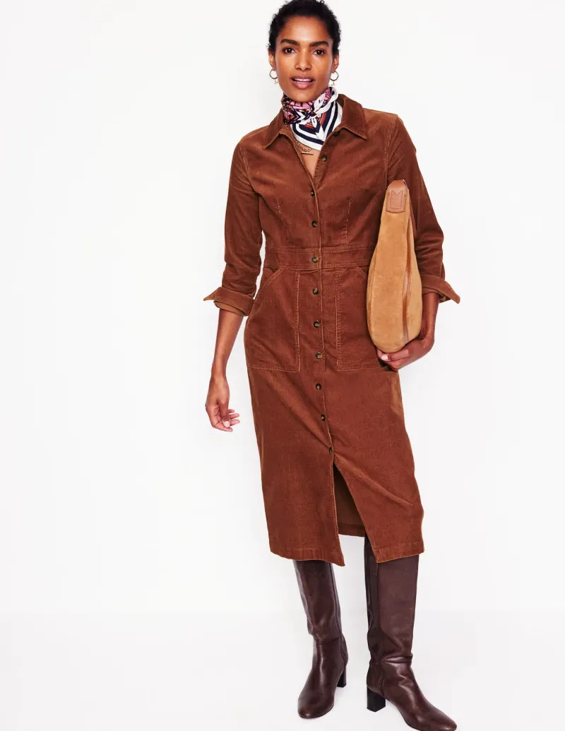 Woman in a rust corduroy button-front shirt dress and dark brown knee boots