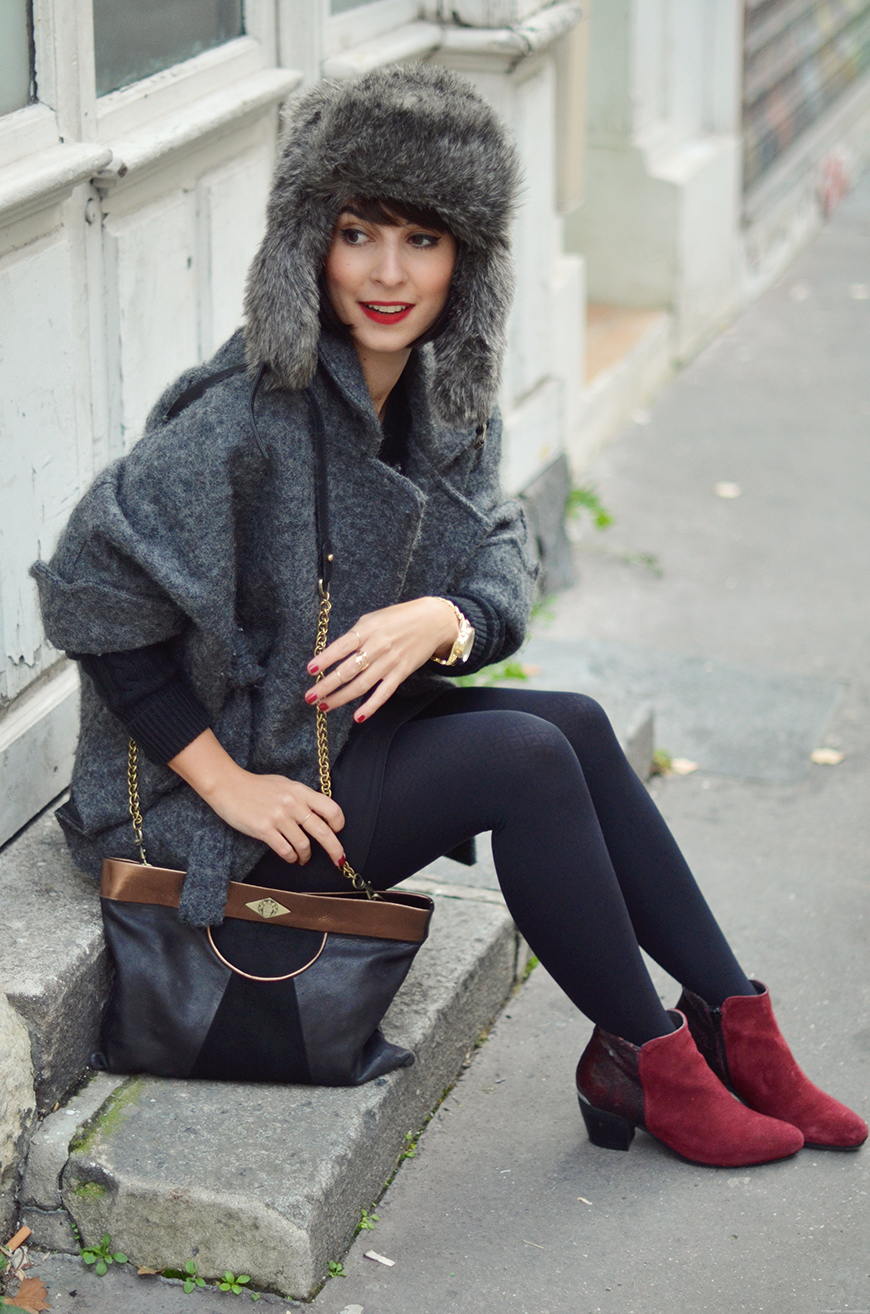 Woman sitting outdoors in a grey faux fur trapper hat, grey wool coat and burgundy boots