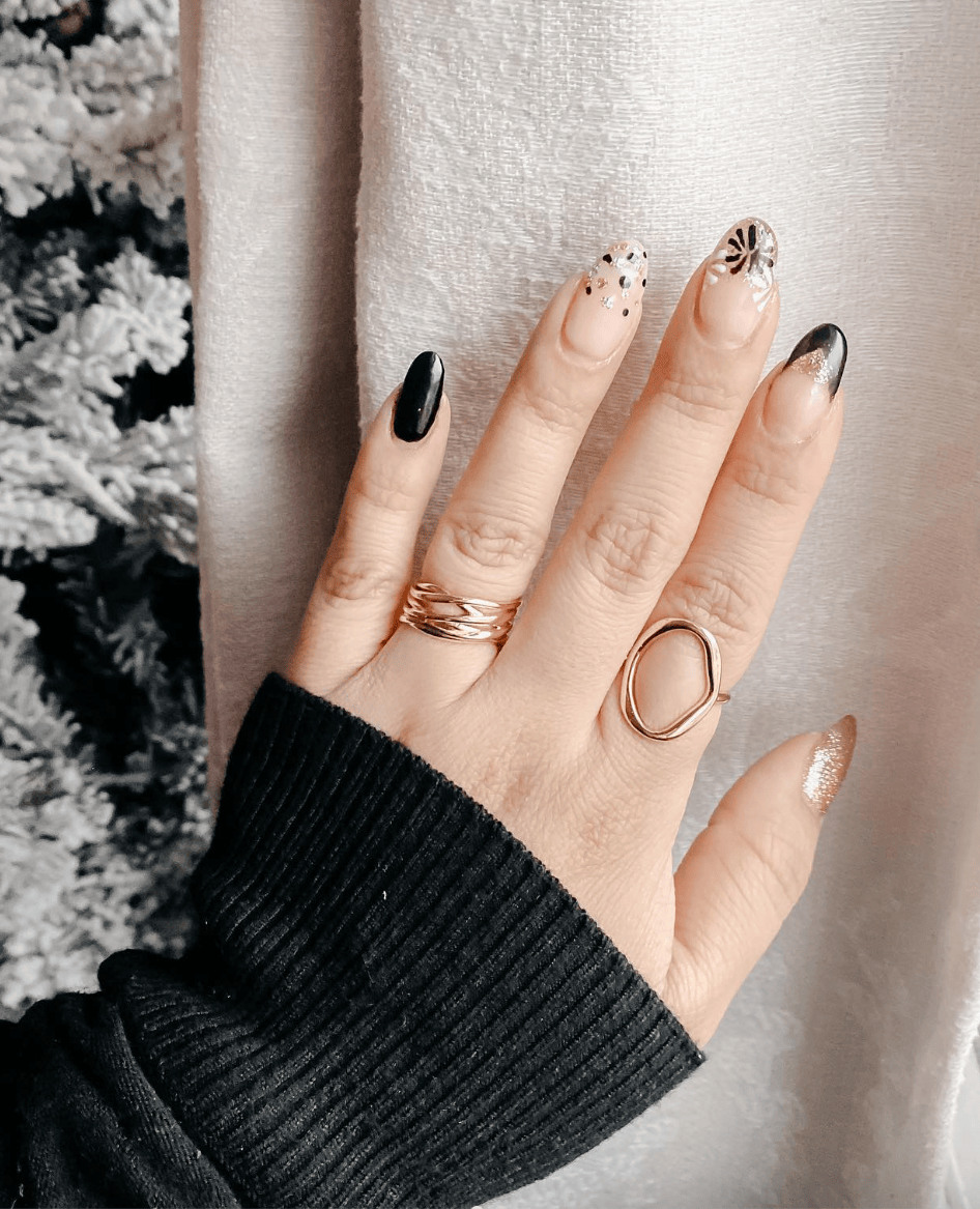 Short oval nails mixing solid black, nude with black French fade, nude with confetti dots and a firework stamp, and a gold glitter thumb