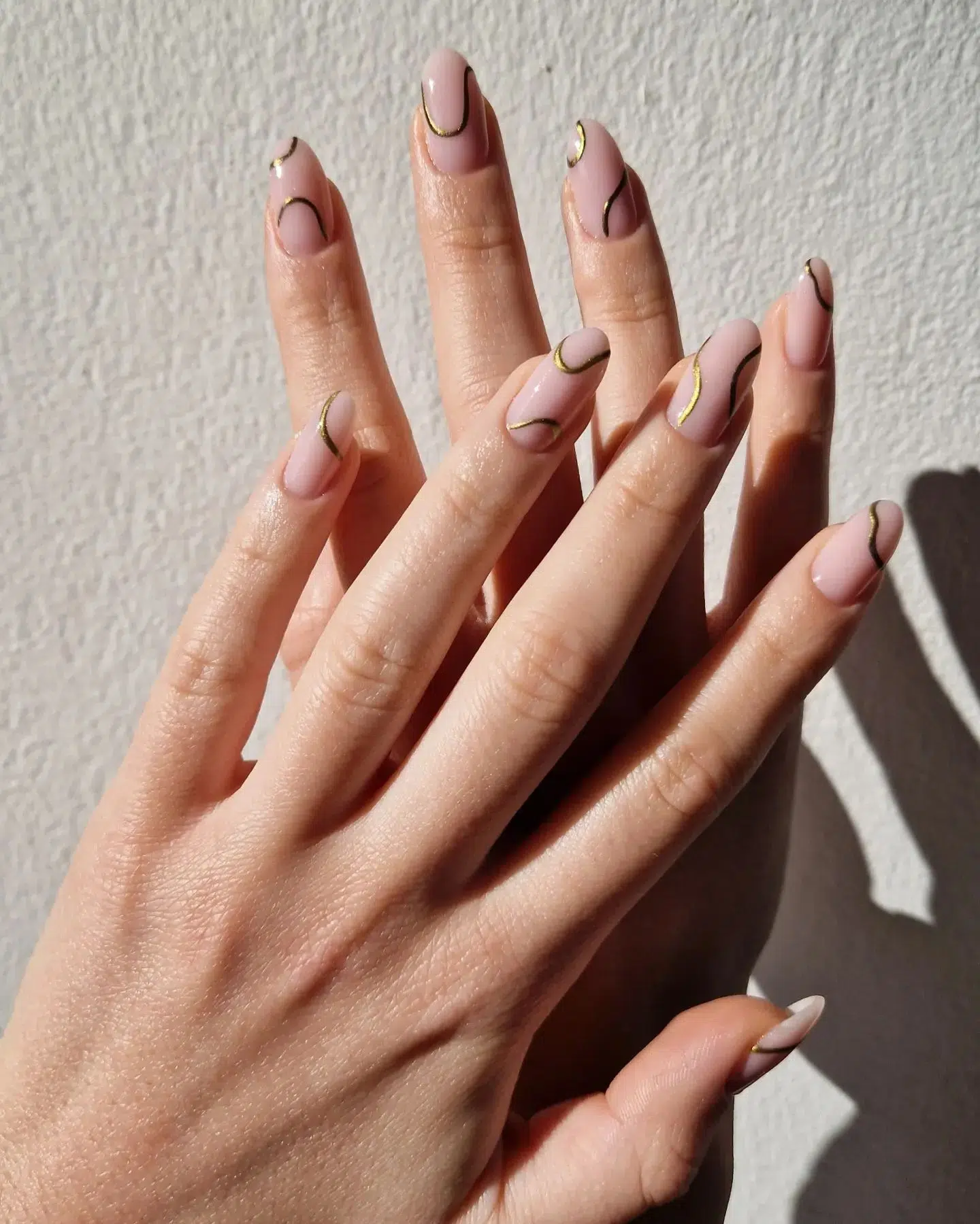 Almond nude nails with delicate gold and black abstract line art