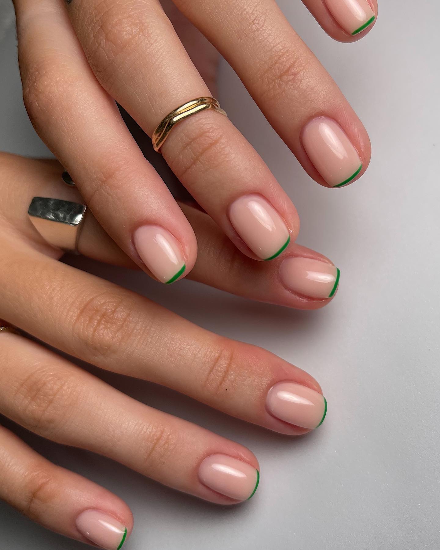Short oval nude nails with thin green micro French tips