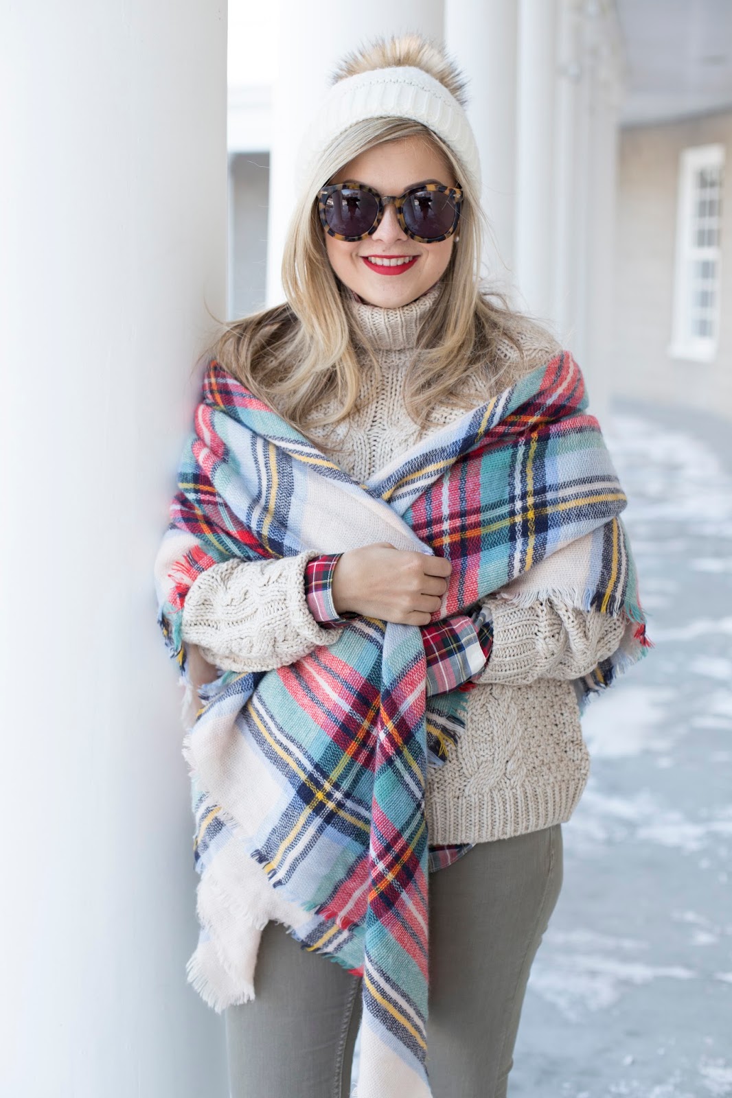 Woman wrapped in a plaid blanket scarf with a wool coat and jeans